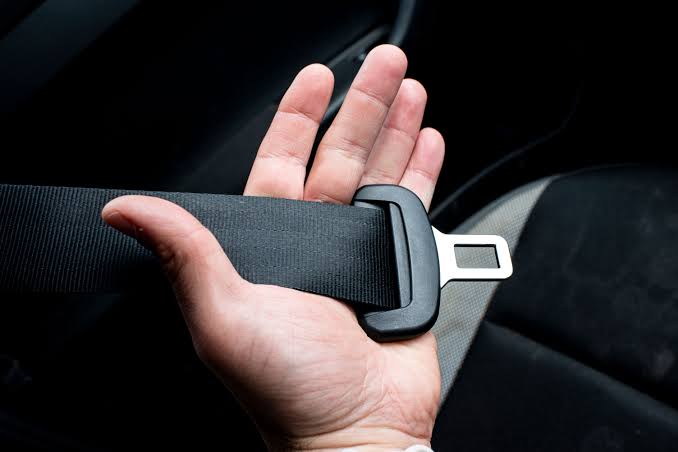 An open hand supporting a length of black seat belt webbing with the metal tongue plate resting across the palm.